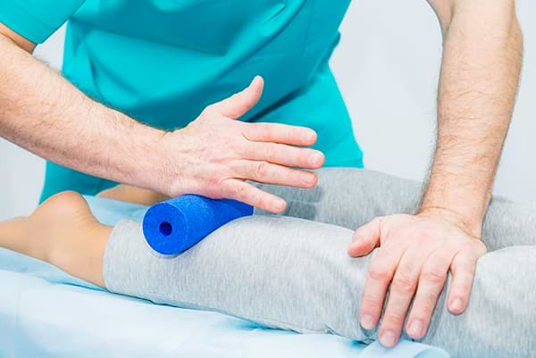 Faszientherapie mit Faszienrolle durch Therapeut bei muskulären Schmerzen an der Wade.
